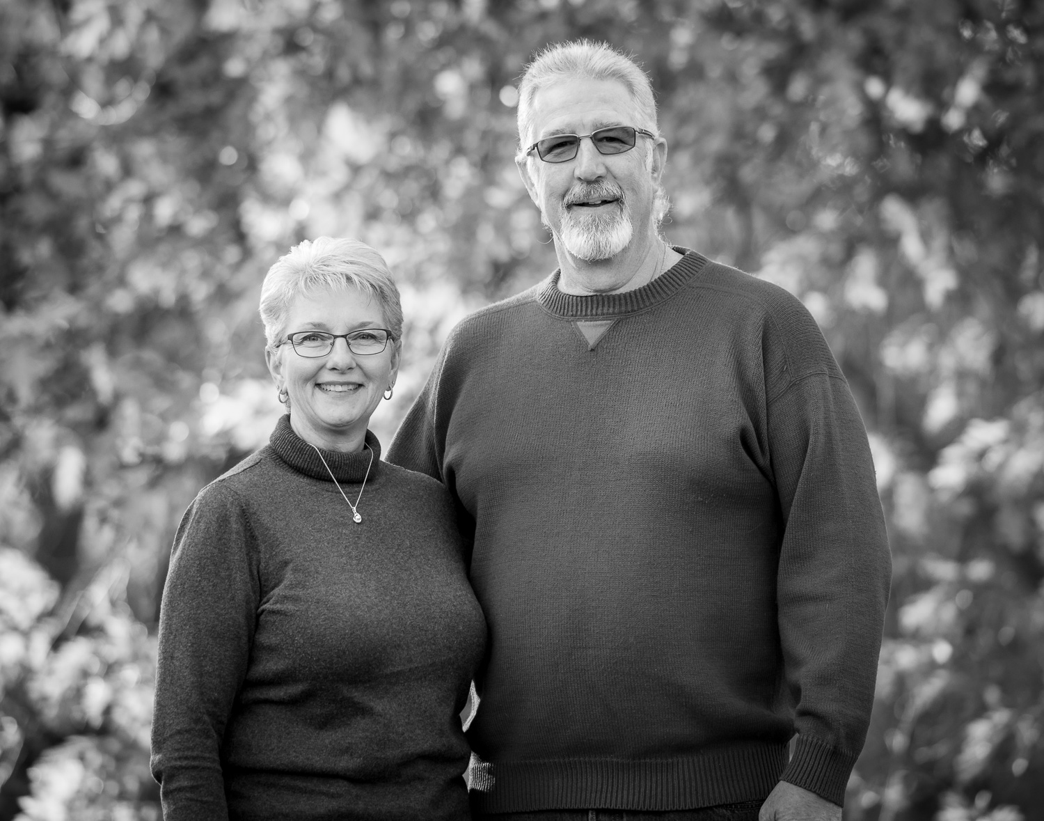 Black and white family photos. A gray-haired husband and wife standing next to each other in the forest.